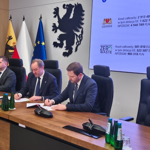 Podpisanie umowy dotyczącej projektu Zero Waste w Gdańsku, przedstawiciele rządu i instytucji, na stole dokumenty i butelki wody. Koszt całkowity projektu wynosi 2 913 409 EUR, w tym dotacja KE 1 622 187 EUR.